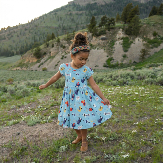 Young girl in a colorful dress standing in a natural landscape with mountains and trees.
