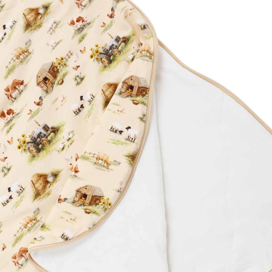 A close-up of a baby blanket or swaddle with a cream background and a detailed farm animal print, showing the reverse side which is plain white.