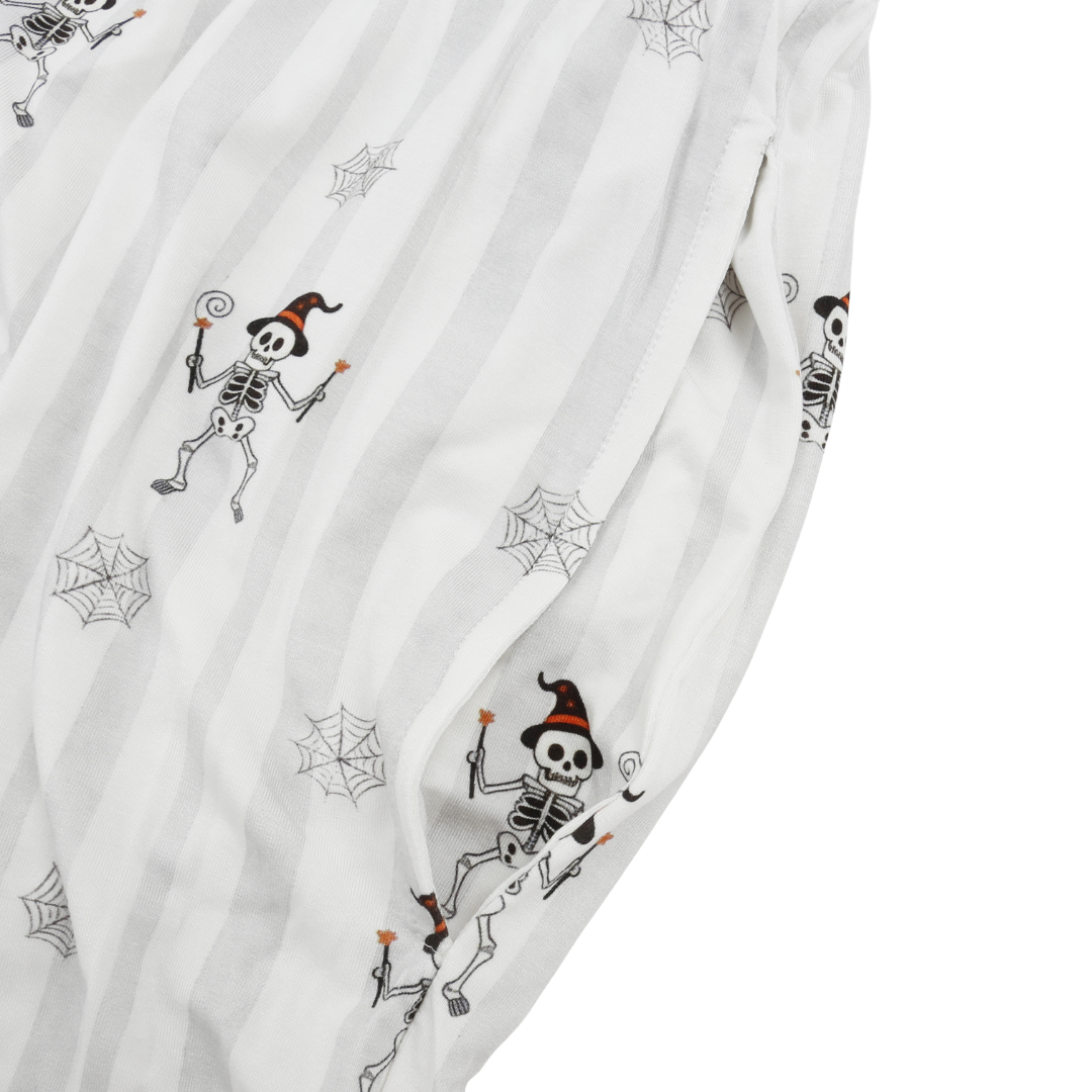 Close-up of a white fabric garment with a Halloween print featuring cartoon skeletons wearing witch hats and spiderwebs.