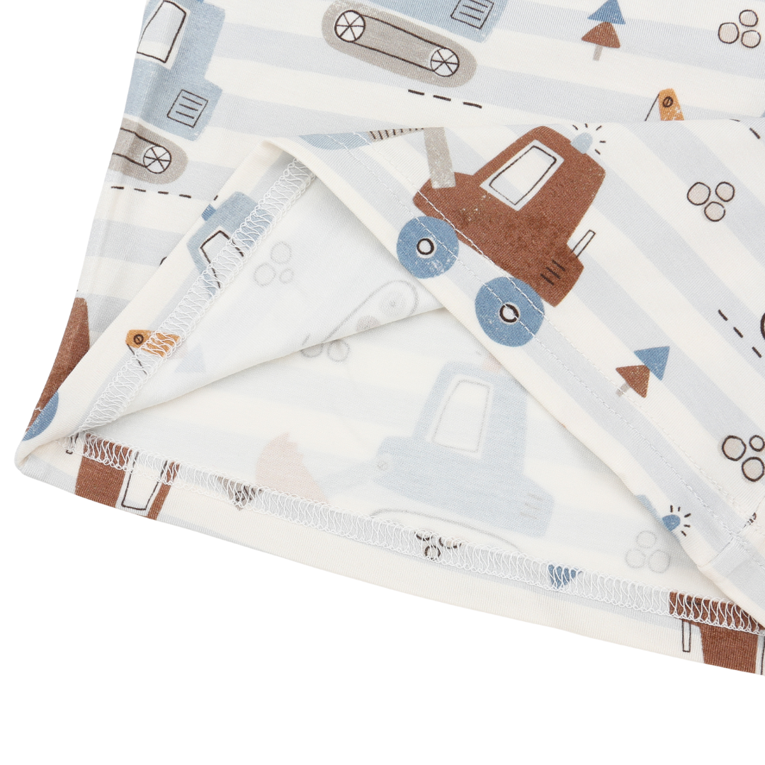 A folded baby blanket with a playful construction vehicle print, featuring brown trucks, blue wheels, and light blue striped patterns on a white background.