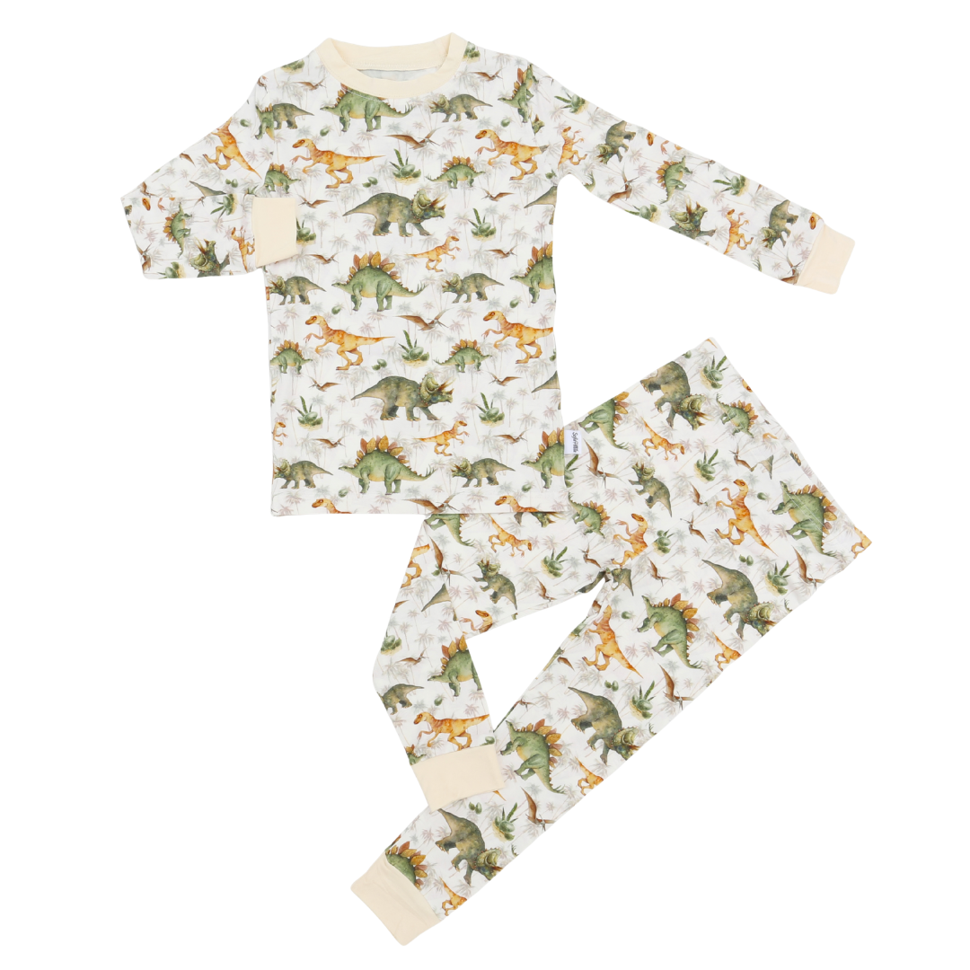 A two-piece children's pajama set featuring a long-sleeve top and matching pants with an all-over dinosaur print on a cream background. The pajamas are decorated with green, orange, and brown dinosaurs, and have solid cream cuffs and collar.