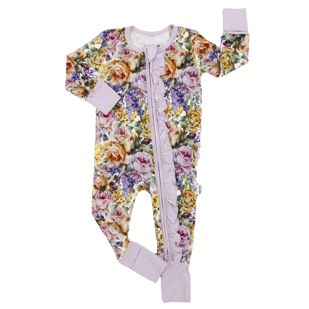 A baby footed sleeper with a lavender ruffle zipper and a multicolor floral print featuring roses and other flowers, shown on a plain white background.
