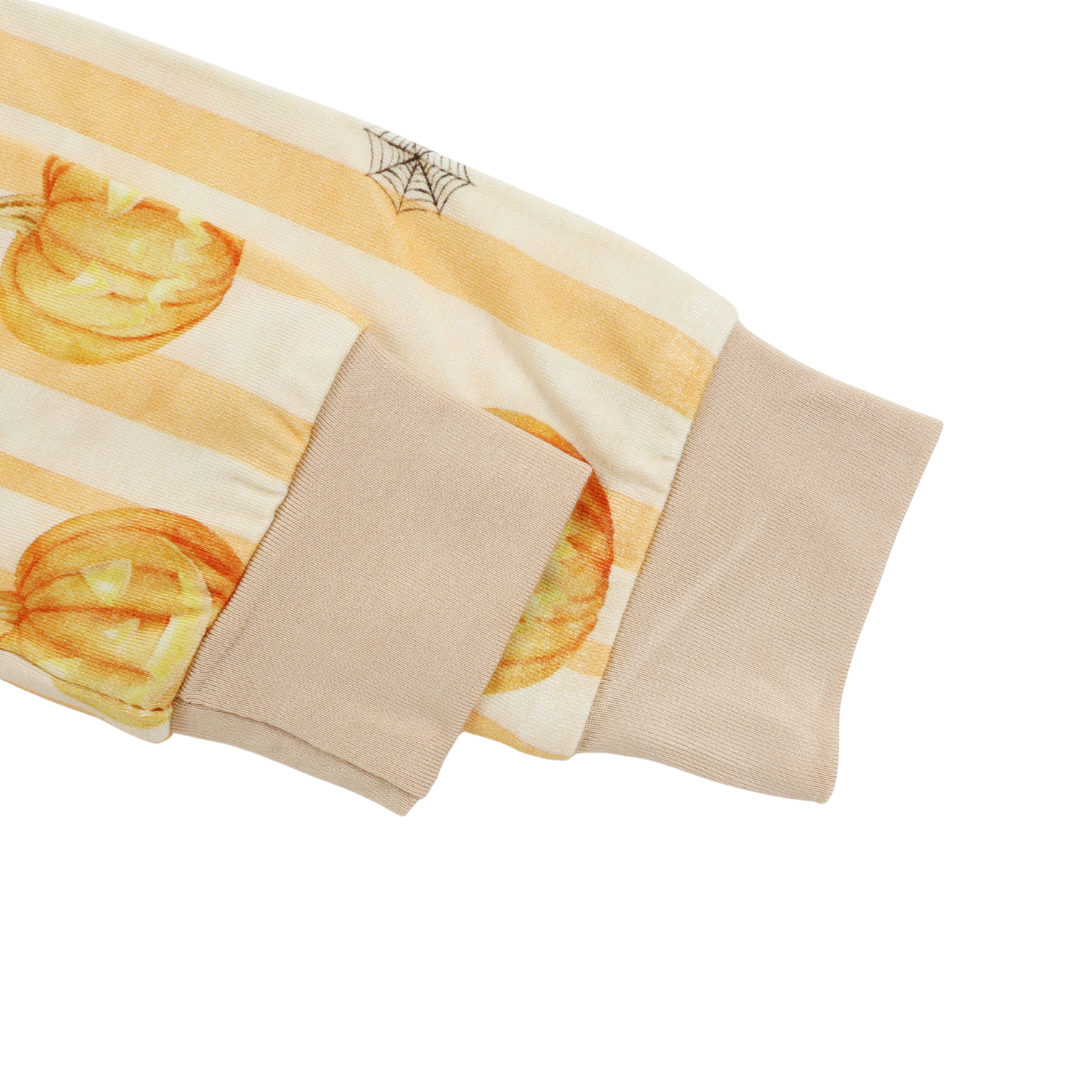 A close-up detail shot of a sleeve or garment cuff featuring a cream and light orange striped pattern with watercolor-style orange pumpkins and a spiderweb motif, finished with solid beige ribbed cuffs.