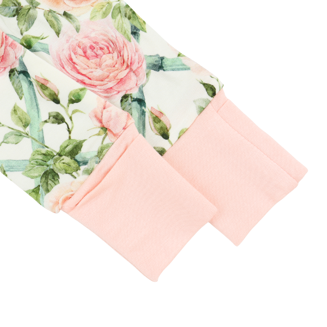 A close-up of a children's long-sleeve top or pajama sleeve with a watercolor-style pink rose floral print on an off-white background and solid light pink ribbed cuffs.