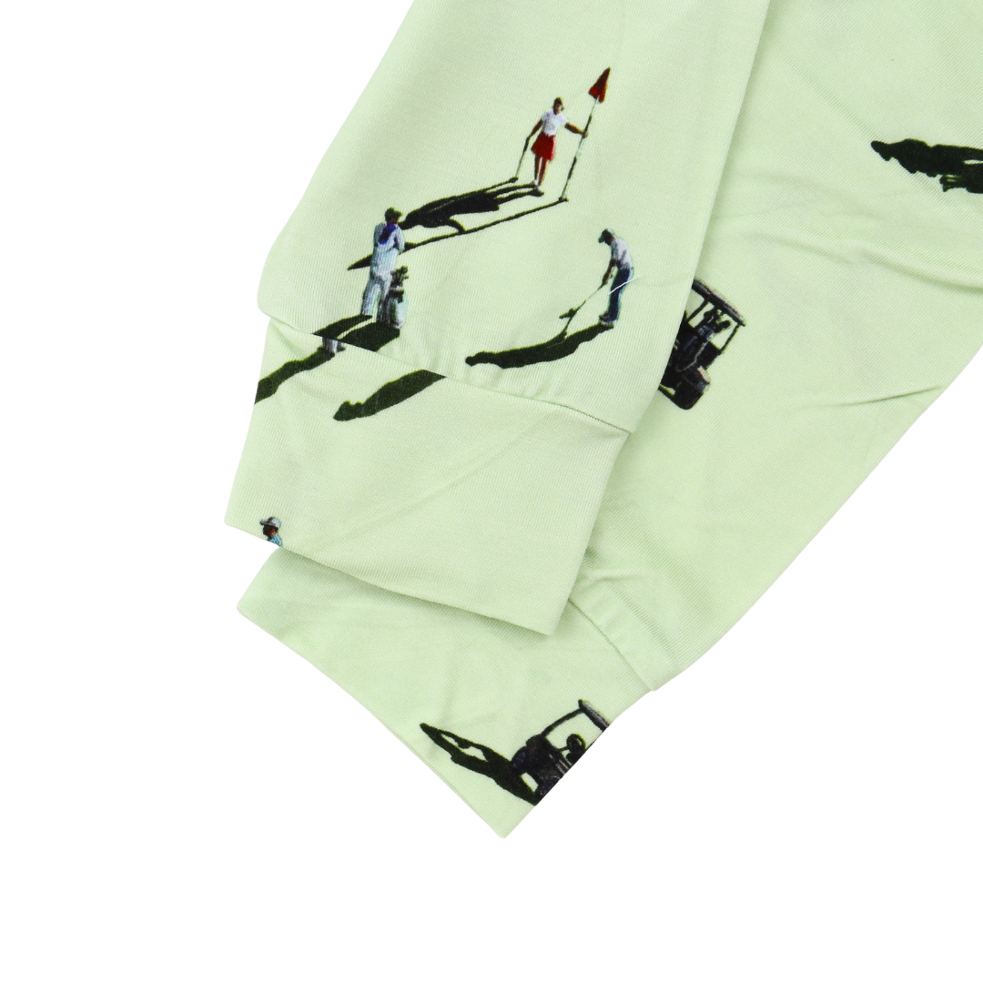 A close-up of a light mint green fabric, likely a sweatshirt or jacket sleeve, featuring a black and white graphic print of people playing golf with golf carts.