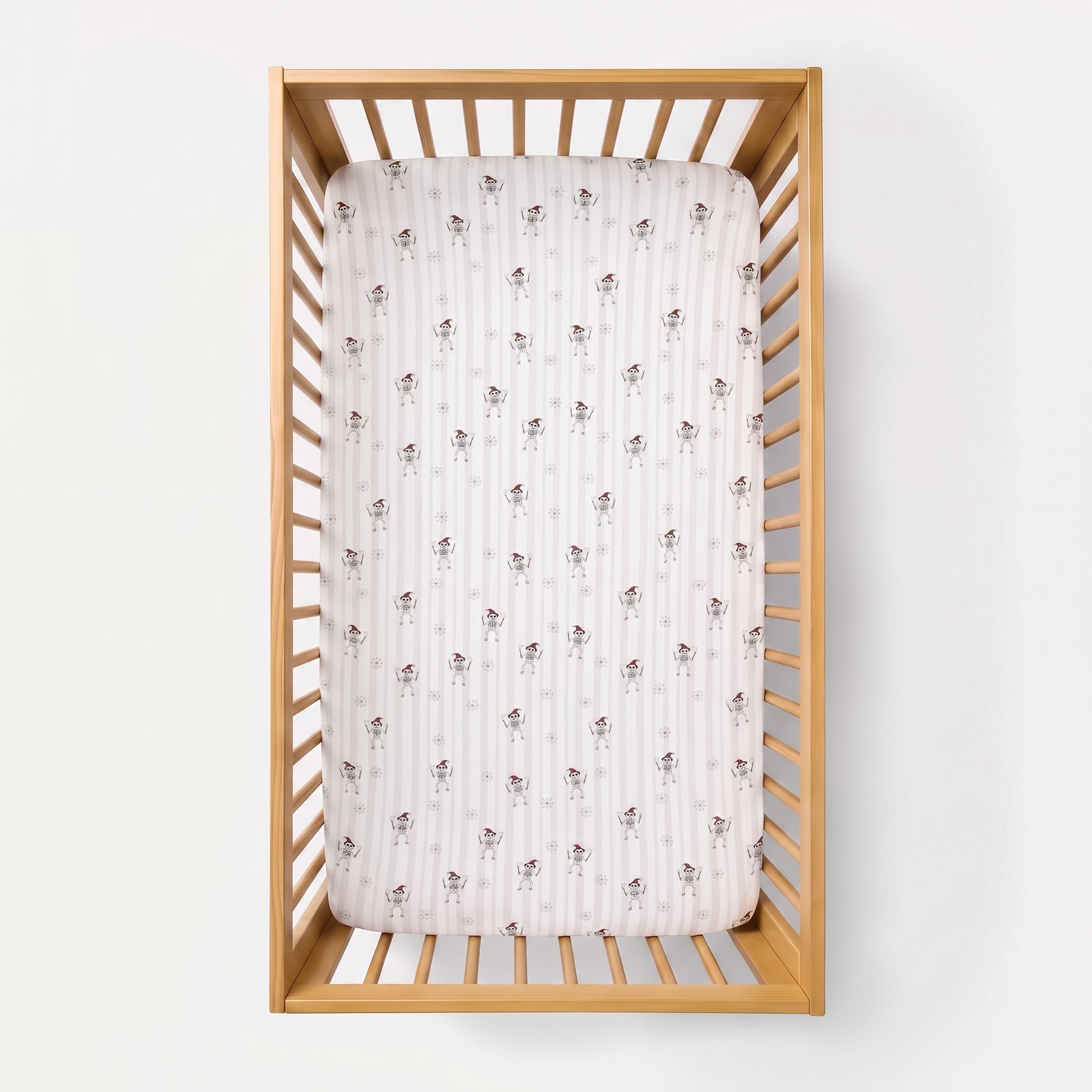 A fitted crib mattress with a white and pink striped pattern and small brown bunny motifs, shown inside a light natural wood crib against a white background.