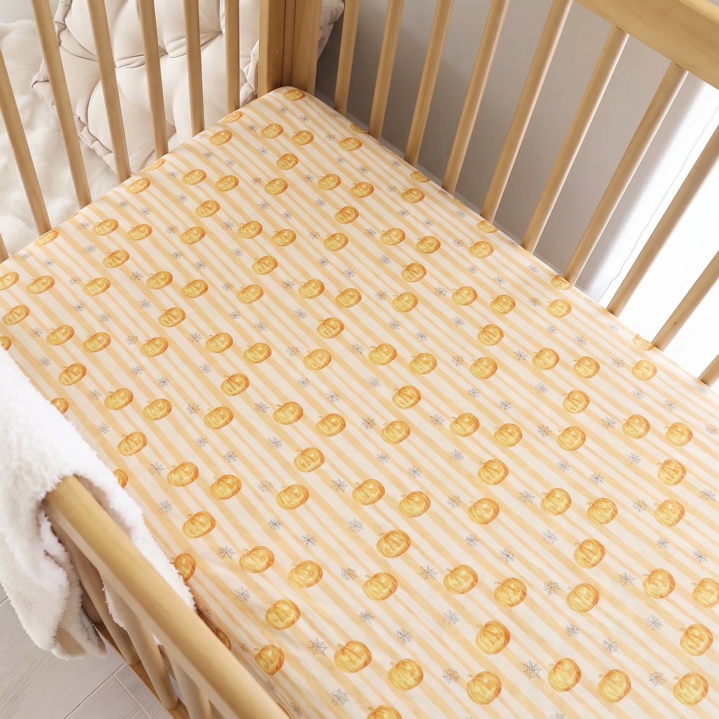 A fitted crib mattress with a yellow and white striped pattern featuring gold coins and small gray stars, shown inside a light wood crib with a white blanket.