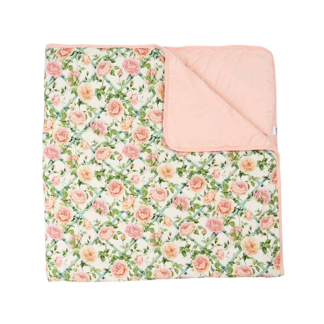 A folded baby blanket featuring a pink and peach rose floral print on an off-white background, with a solid pale pink reverse side.