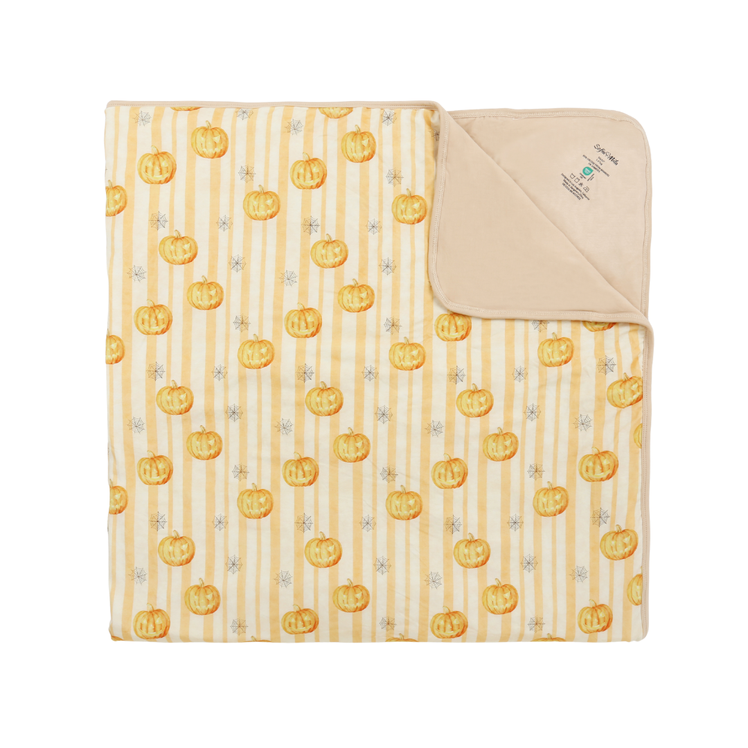 A folded baby blanket with a cream and yellow vertical stripe pattern, decorated with orange jack-o'-lanterns and small gray stars. The soft, fleece-like reverse side is folded over to show the beige lining, with a small sewn label visible.