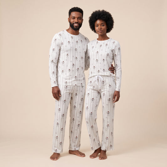 A man and a woman standing barefoot and wearing matching long-sleeve pajama sets with a small floral print on a white and beige striped background, against a solid beige studio backdrop.