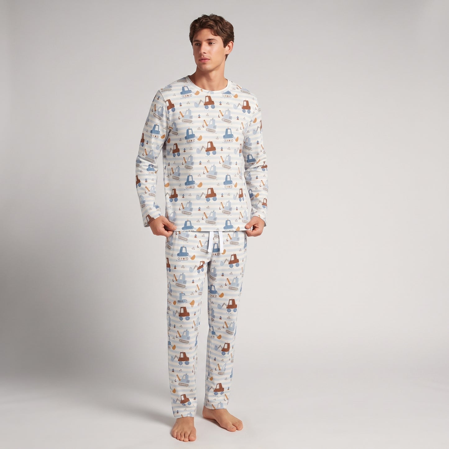 A man modeling a matching long-sleeve pajama shirt and pants set with an all-over whimsical boat pattern on a white background, photographed in a studio setting.