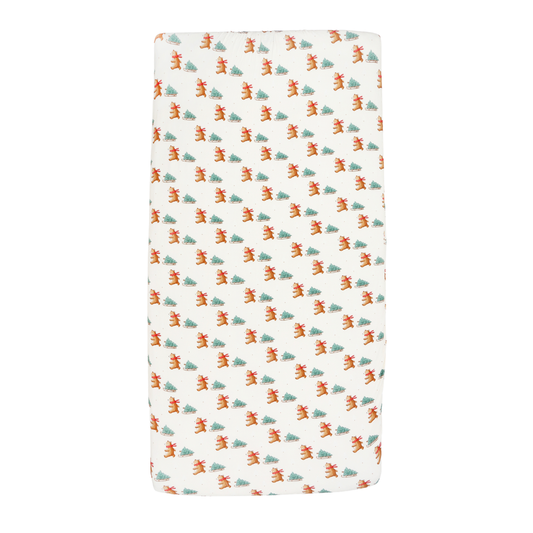 A rectangular baby blanket or swaddle with an all-over repeating pattern of small orange foxes and green pine trees on a warm off-white background.