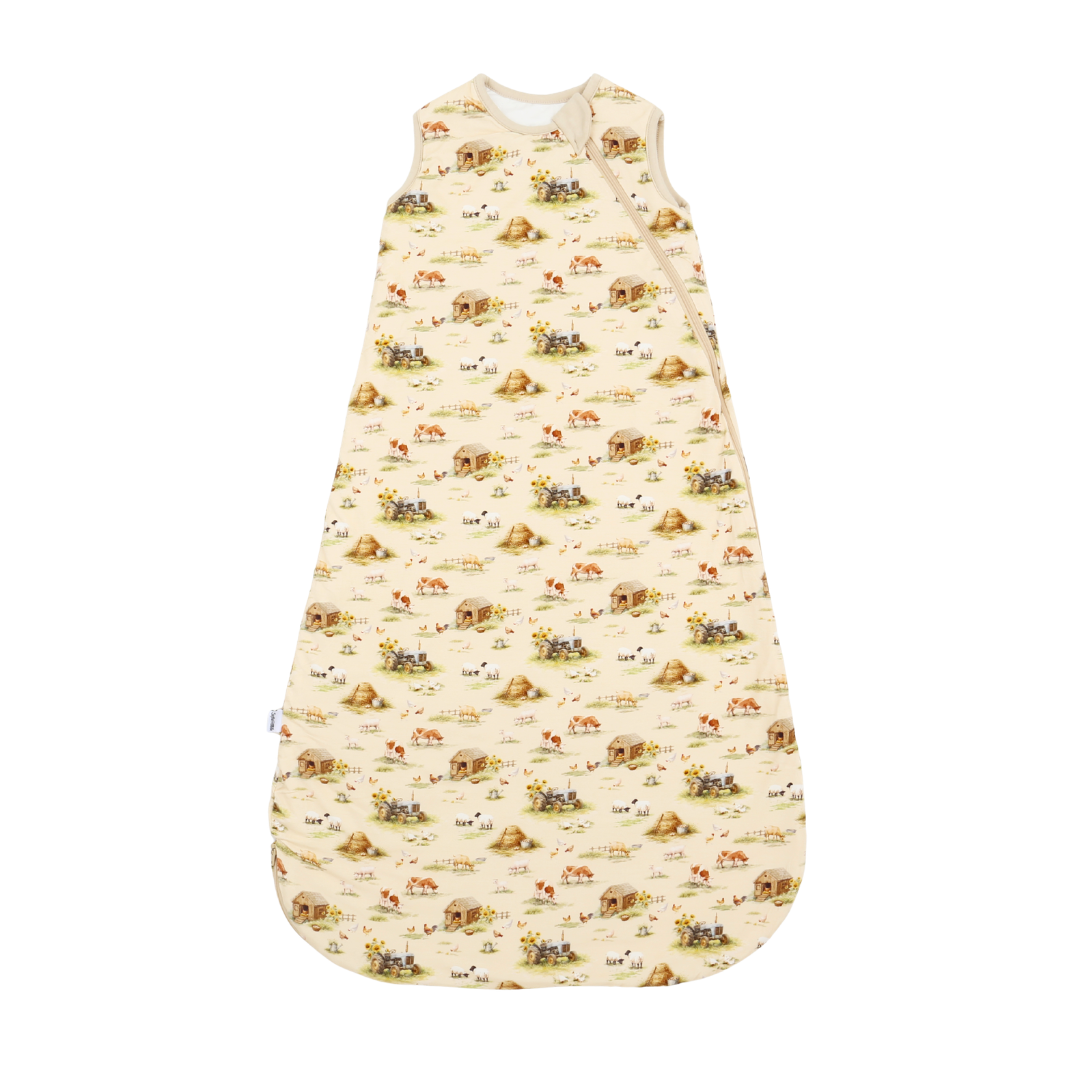 A sleeveless baby sleep sack with a cream-colored background and an all-over whimsical pattern of farm animals, including cows, sheep, chickens, and horses, in brown, yellow, and green.