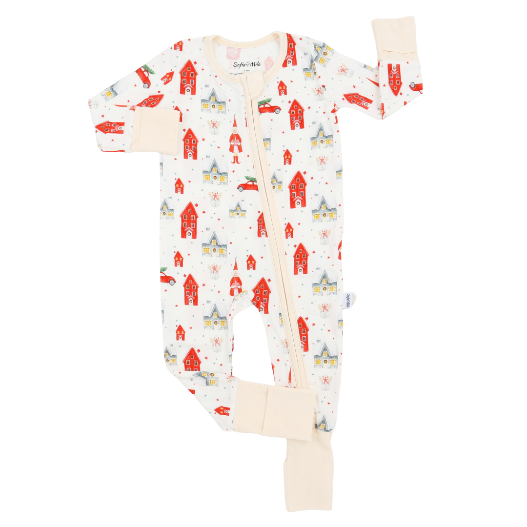 A baby long-sleeve footless zip-up sleeper with a festive winter print of red houses, yellow cars, and blue snow globes on a cream background, featuring beige ribbed cuffs and ankle cuffs.