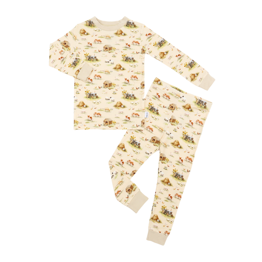 A two-piece children's pajama set featuring a long-sleeve top and matching pants in a warm cream color with a playful all-over print of cartoon animals and landscapes.