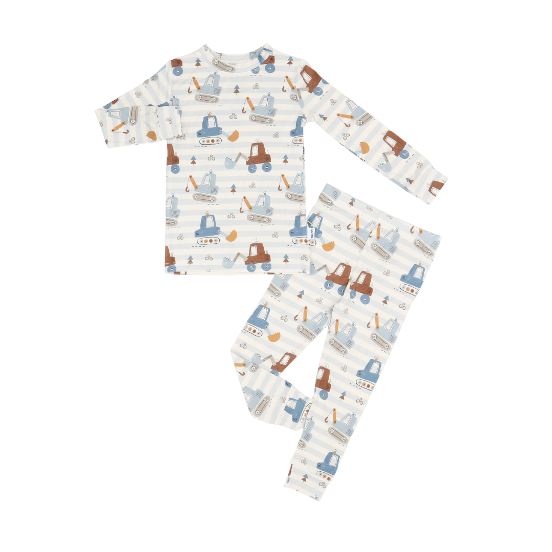A two-piece children's pajama set with a long-sleeve top and matching pants, featuring a playful construction vehicle pattern with blue tractors, brown excavators, and yellow cranes over a white and light blue striped background.