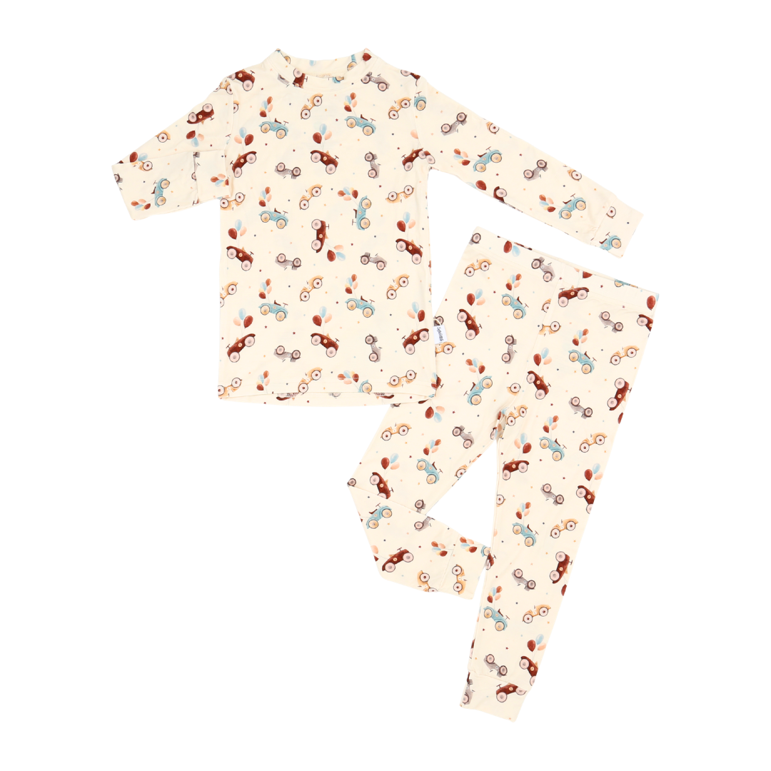 A two-piece long-sleeve pajama set featuring a cream-colored base with an all-over pattern of small colorful toy cars in red, blue, and brown, laid flat on a white background.