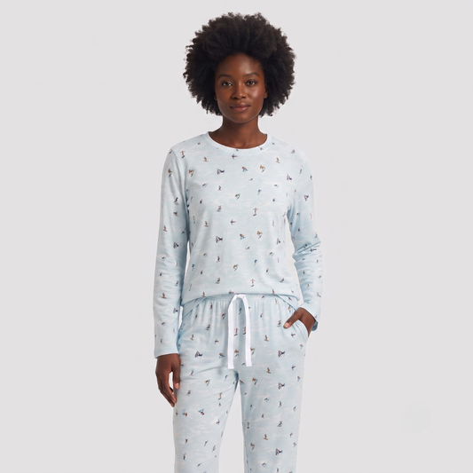 A woman modeling a light blue long-sleeve pajama top and matching pants set with a small all-over print, photographed against a plain light gray studio background.