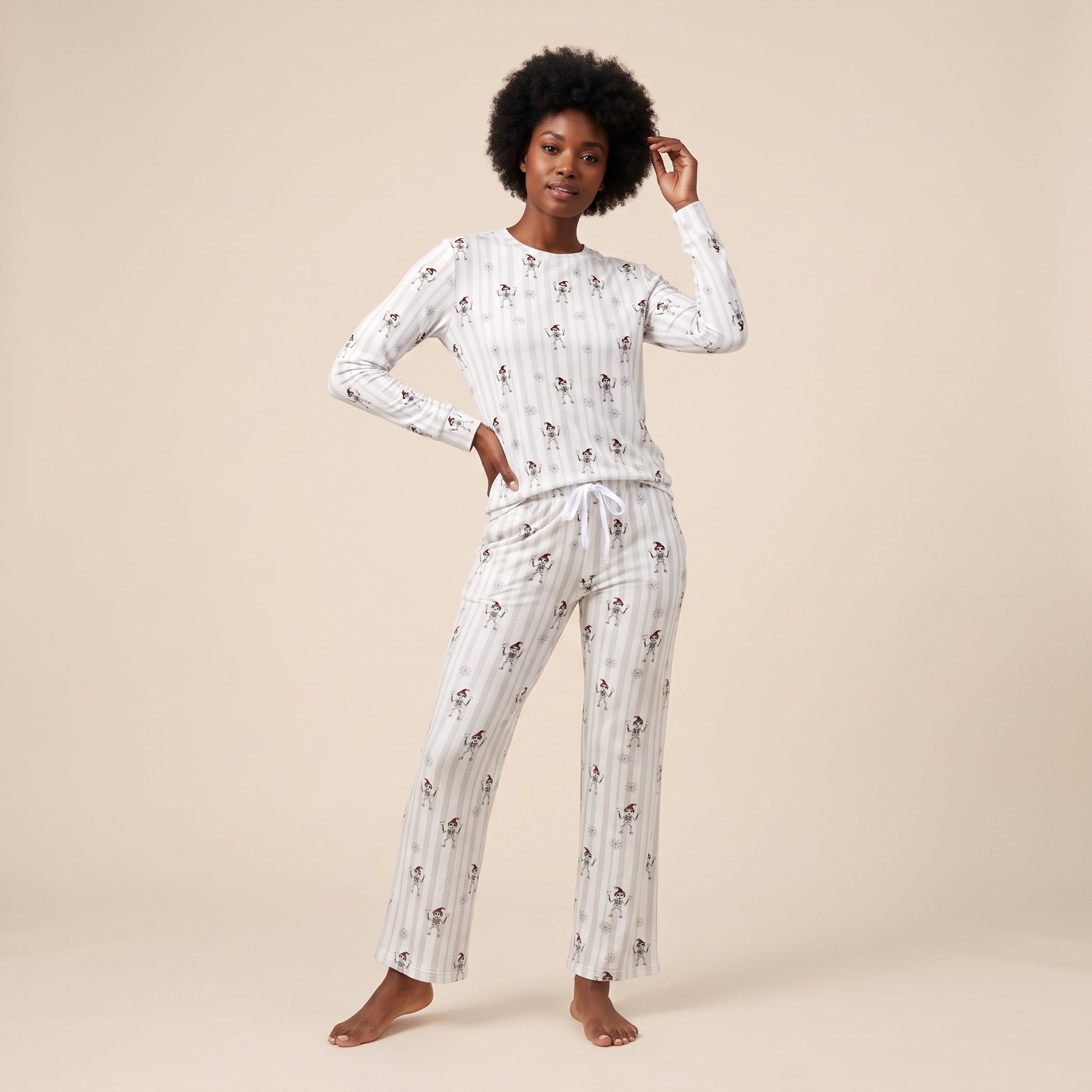 A woman modeling a two-piece long-sleeve pajama set with a white base, thin vertical gray stripes, and a small all-over floral print, set against a solid beige studio background.