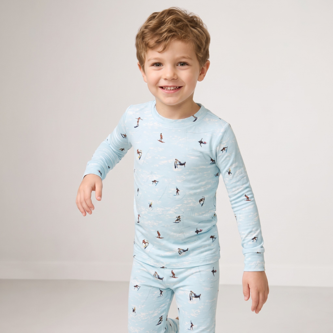 A young boy smiling and wearing a light blue long-sleeve pajama top and matching pants with a small dog print, photographed against a plain light gray studio background.