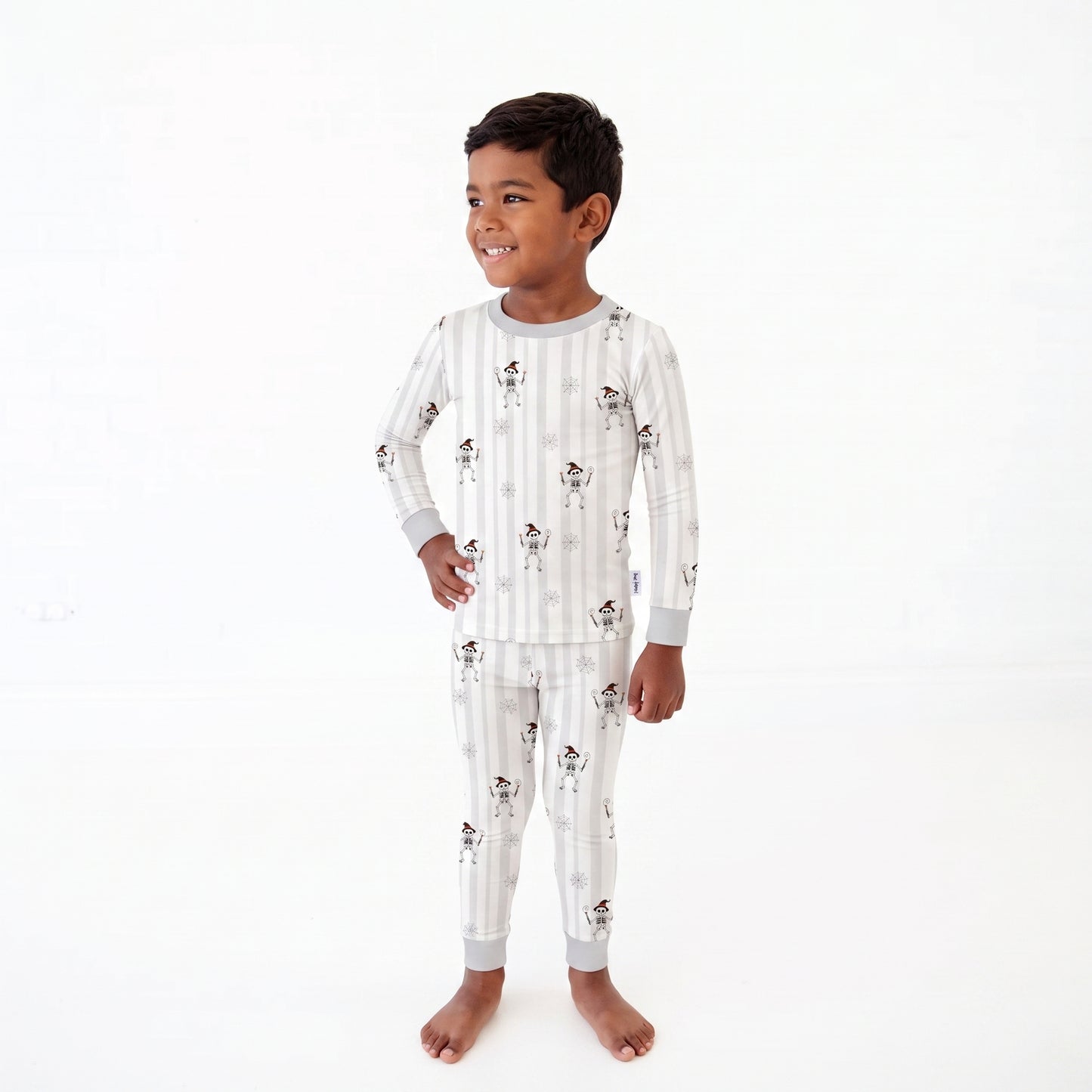 A young boy wearing a long-sleeve pajama set with vertical white and light gray stripes and a small dog print, standing against a plain white background.