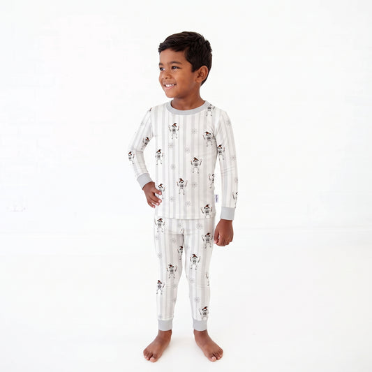 A young boy wearing a long-sleeve pajama set with vertical white and light gray stripes and a small dog print, standing against a plain white background.