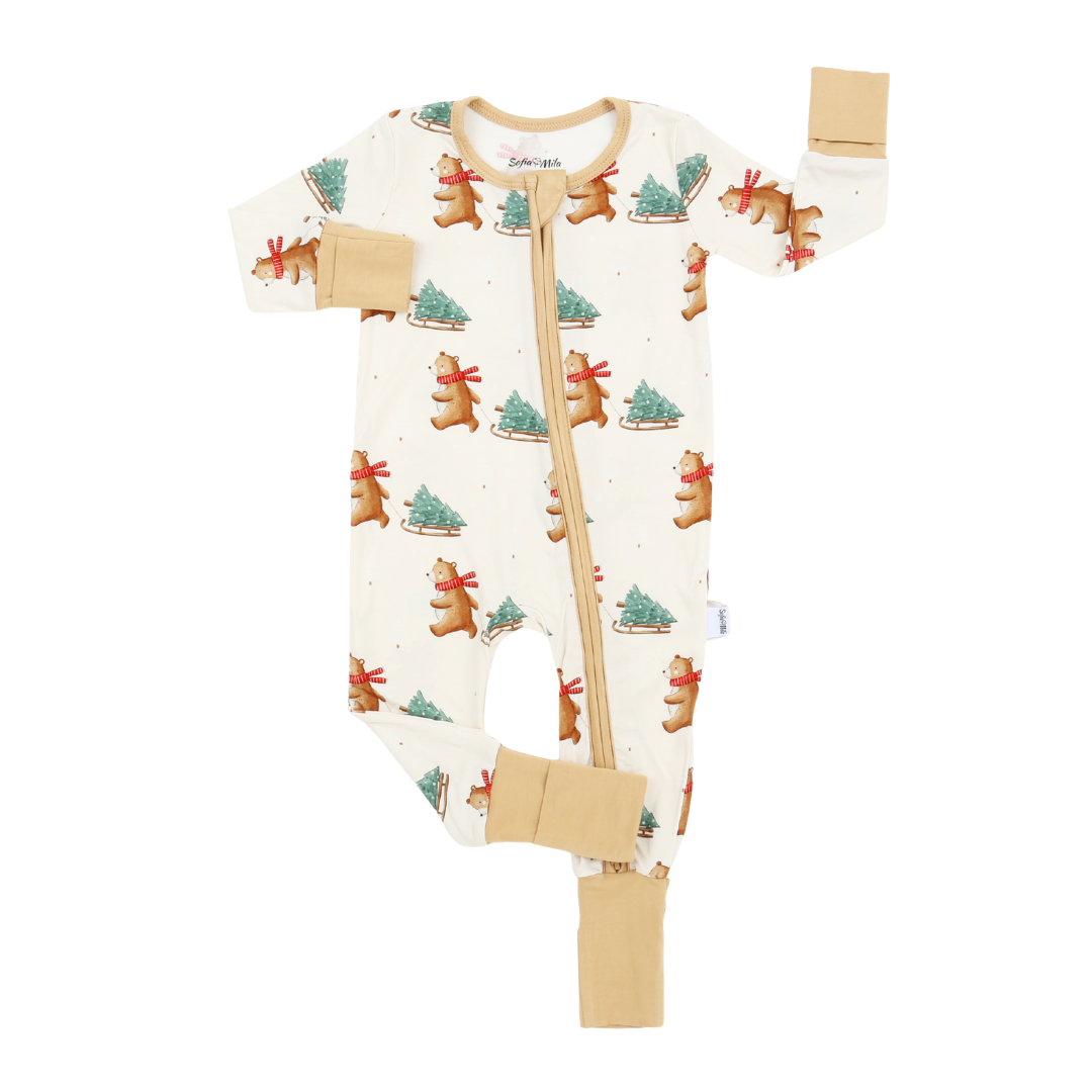 An off-white baby footless one-piece sleeper with a front zipper, featuring a repeating pattern of gingerbread bears and Christmas trees, with tan accents on the cuffs, collar, and zipper trim.