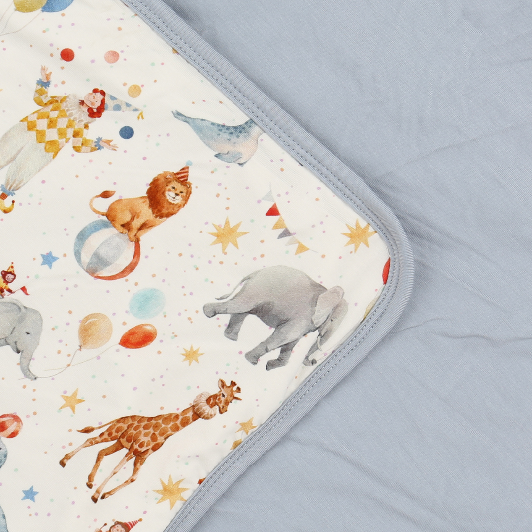 Baby blanket with circus-themed design featuring animals and stars on a light blue background.