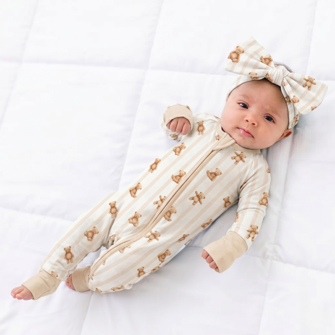 Baby in a cream-colored outfit with bear patterns and matching headband on a white background