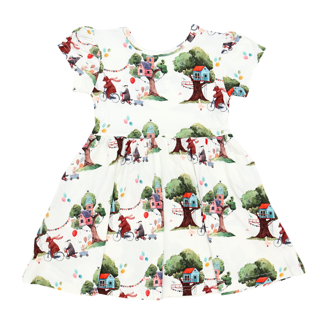 Children's dress with a colorful pattern of houses, trees, and people on a white background