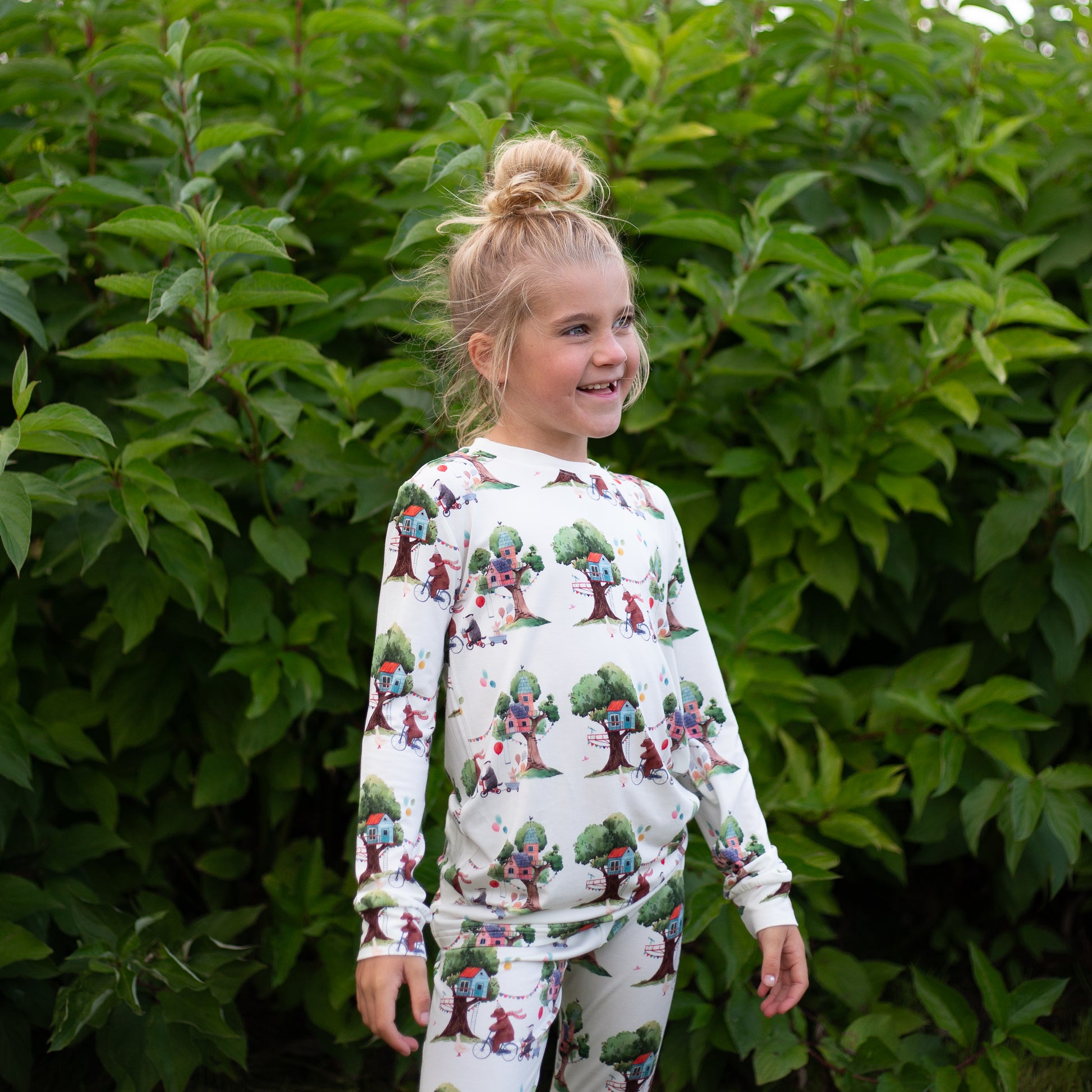 Child wearing a patterned outfit standing in front of green foliage