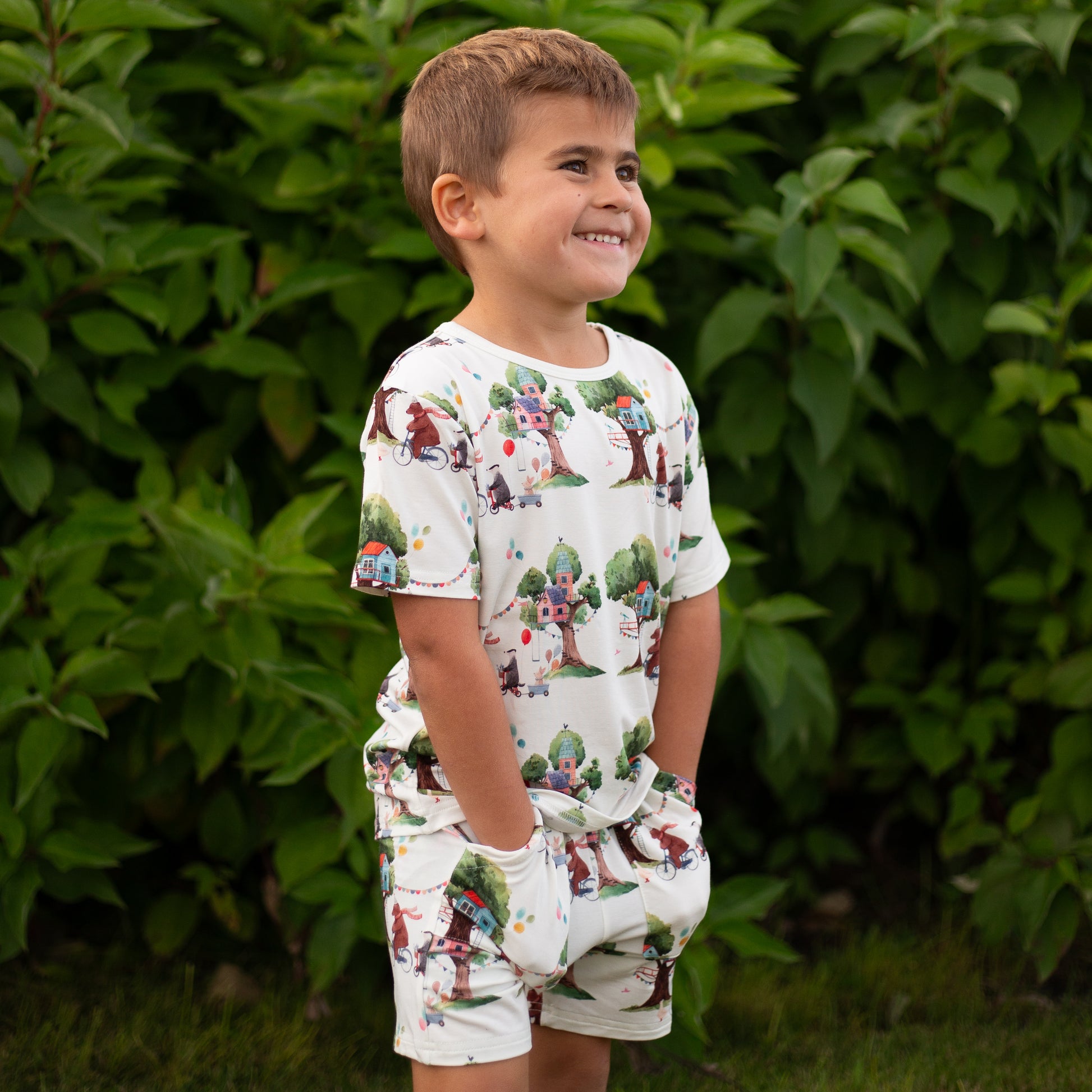 Child wearing a patterned romper standing in front of green foliage