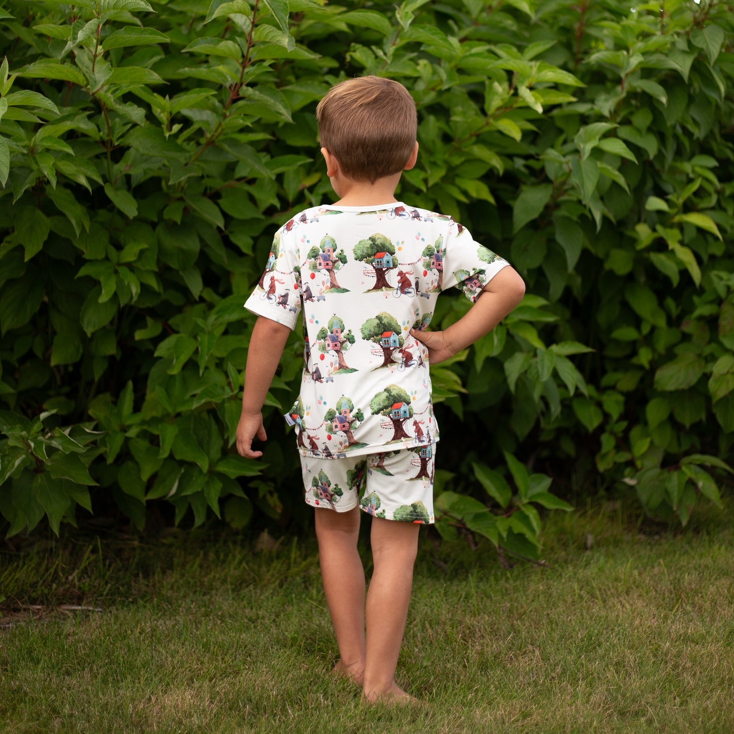 Child wearing a patterned outfit standing in front of green foliage