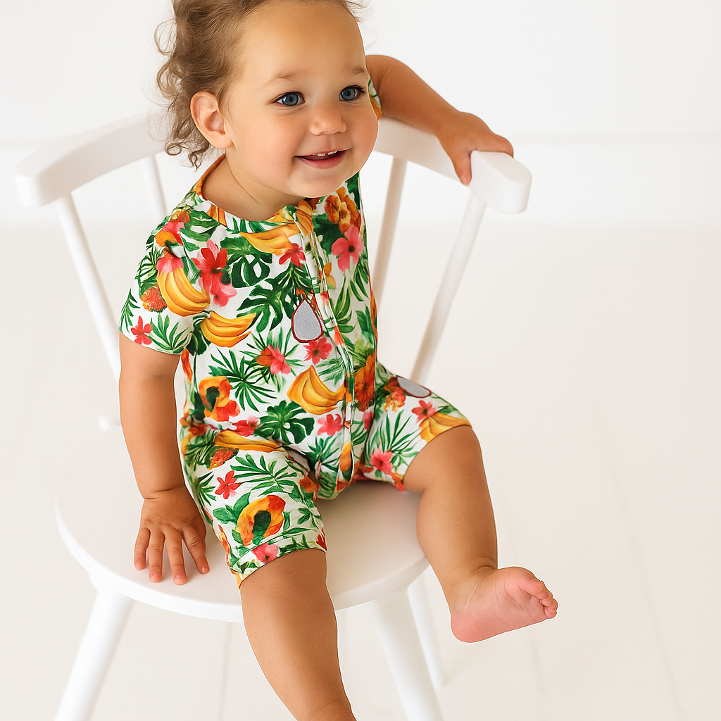 Child wearing a colorful tropical-themed romper sitting on a white chair.