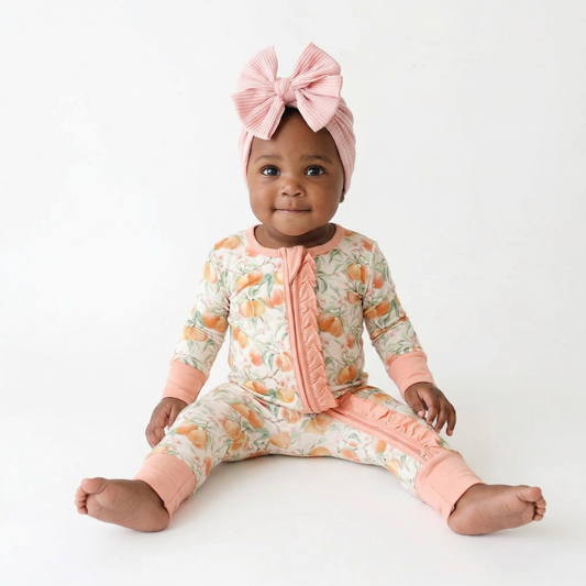 Baby wearing a floral onesie with pink accents and a matching headband on a white background