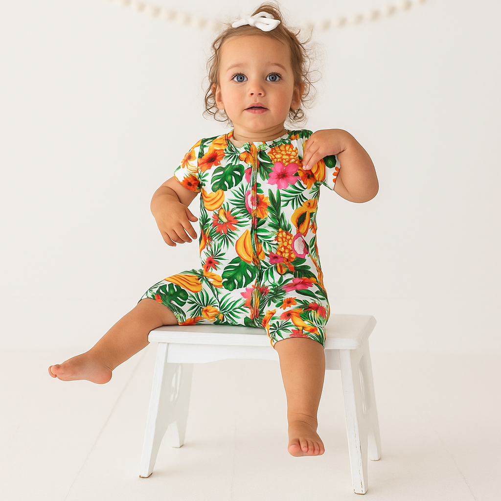 Child wearing a colorful tropical-themed romper sitting on a white stool against a light background