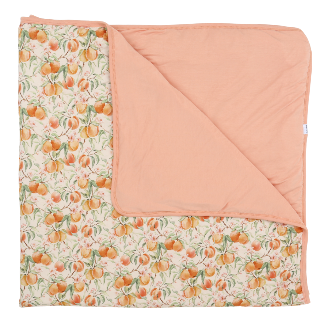 Blanket with peach pattern on one side and solid peach color on the other, folded neatly.