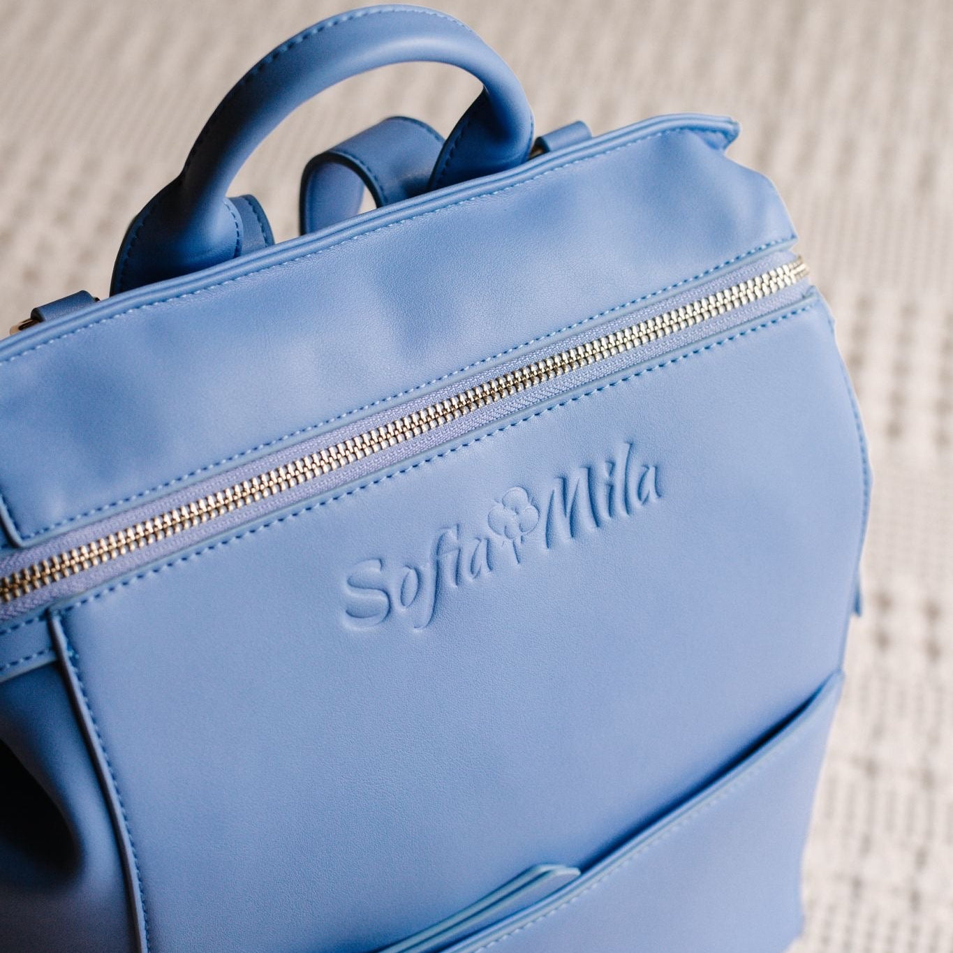 Blue backpack with 'Sofia Mills' branding on a textured surface