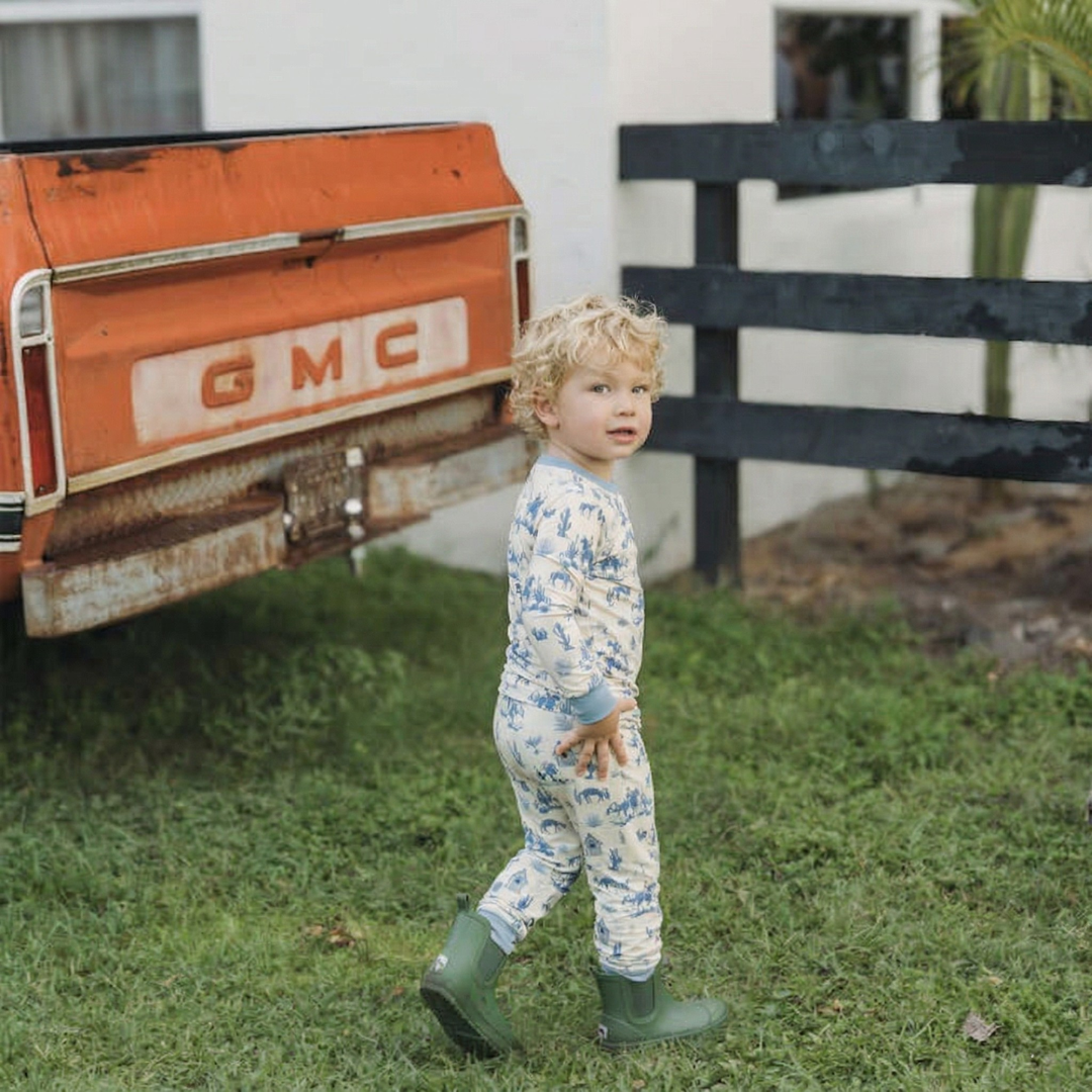 Child in a Western onesie and green boots standing in front of an old GMC truck.