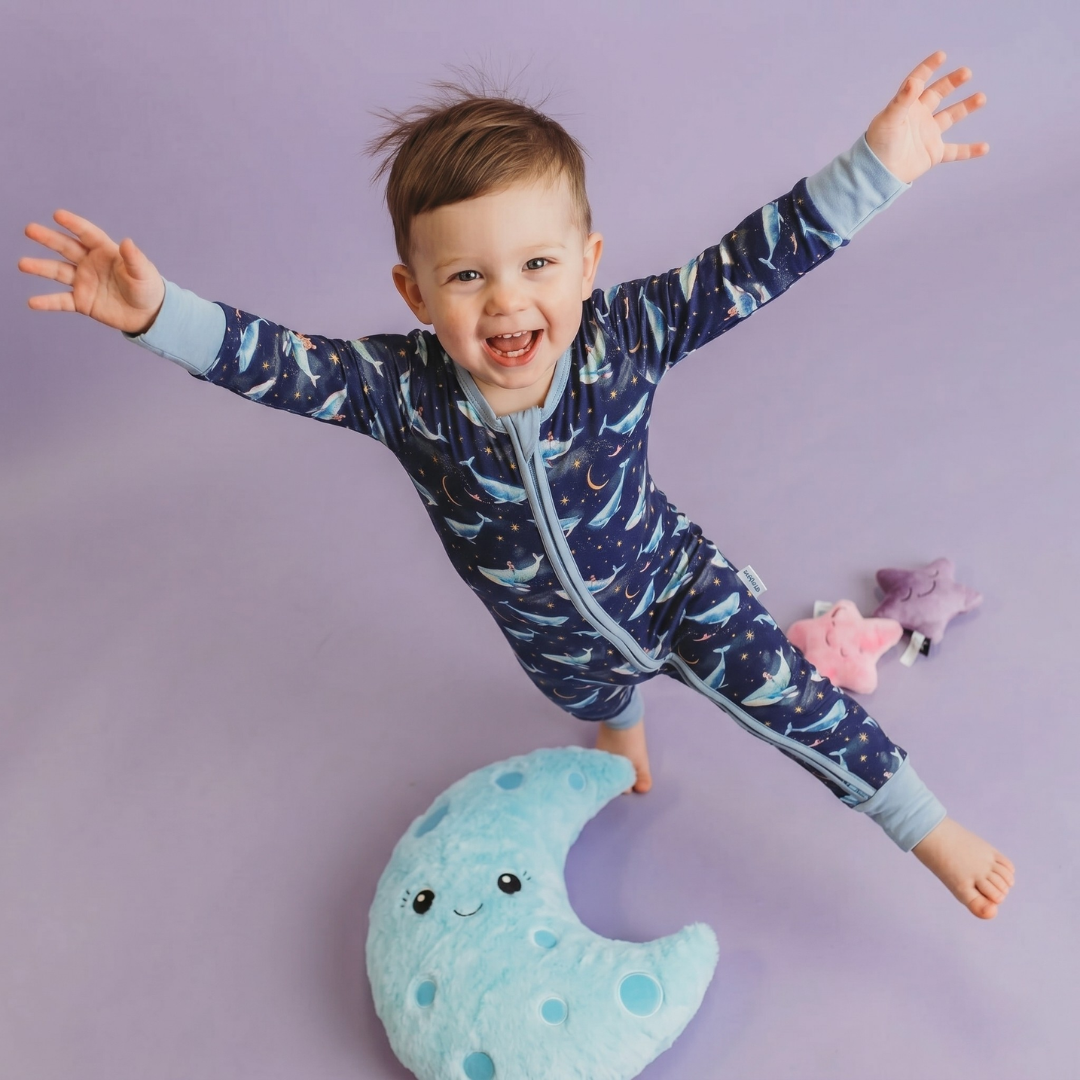 Child wearing a blue space-themed onesie with arms outstretched on a purple background
