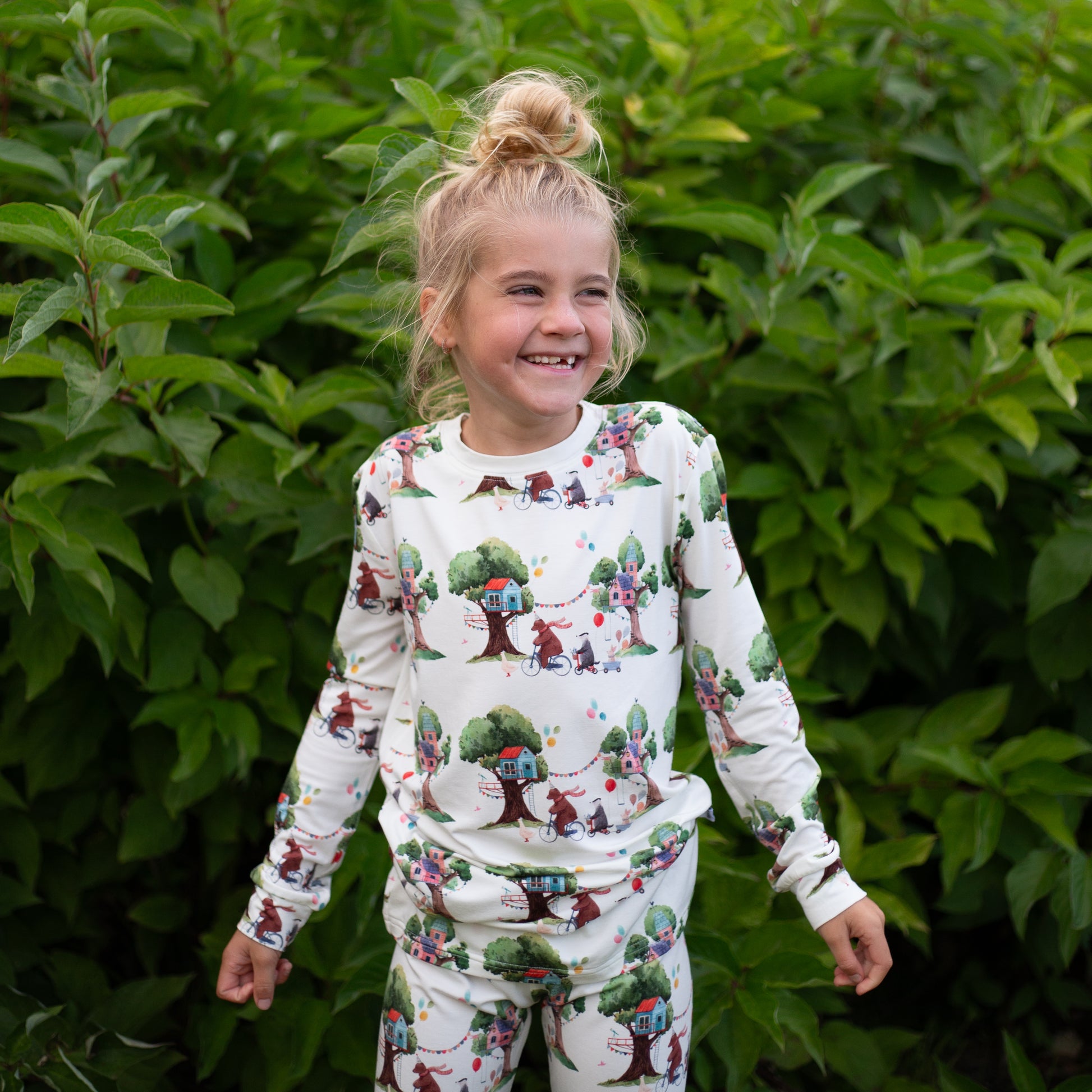 Child wearing a patterned outfit standing in front of green foliage