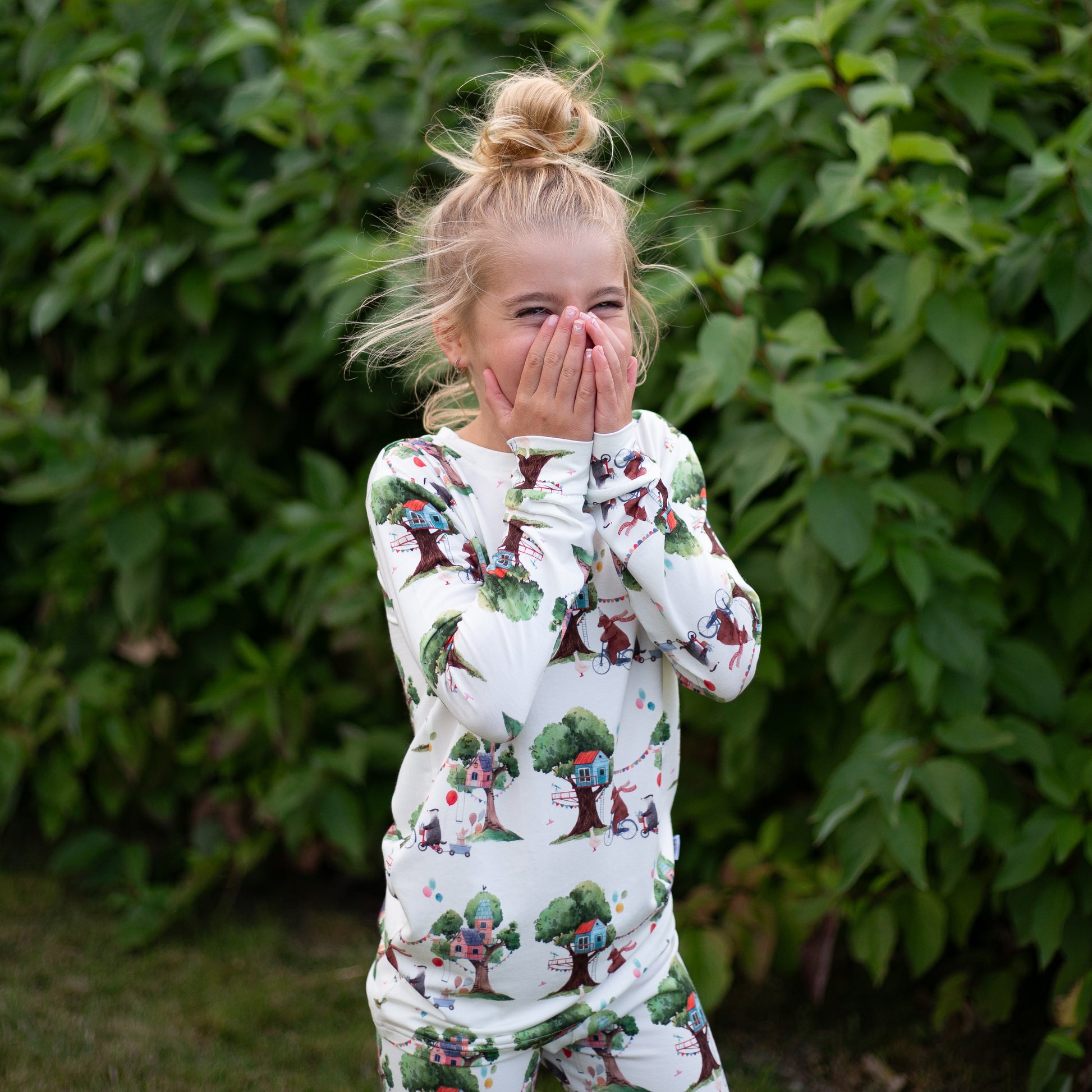 Child wearing a patterned outfit standing outdoors with greenery in the background