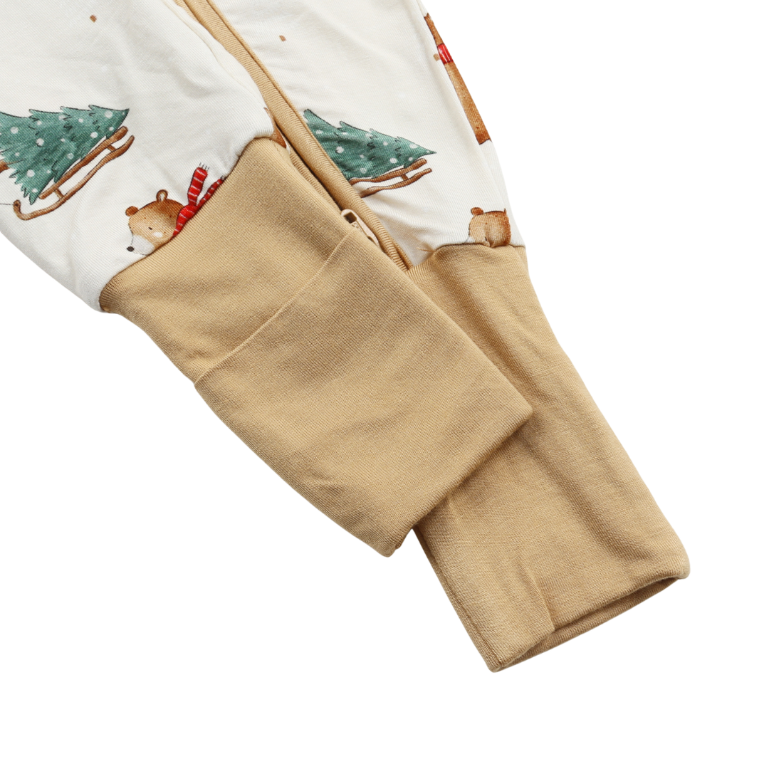 Close-up of a baby footed sleeper with a white Christmas print featuring green trees, bears, and sleds, folded to show a soft tan fleece lining.