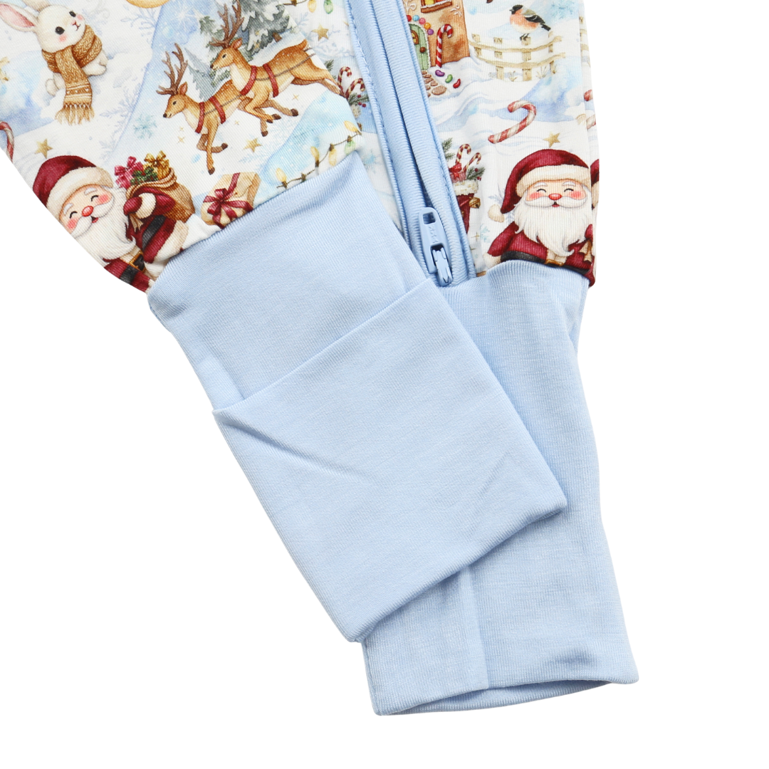 Close-up of a baby one-piece sleeper or footie with a light blue zipper and matching light blue cuff, featuring a Christmas print with Santa Claus and reindeer on a white background.