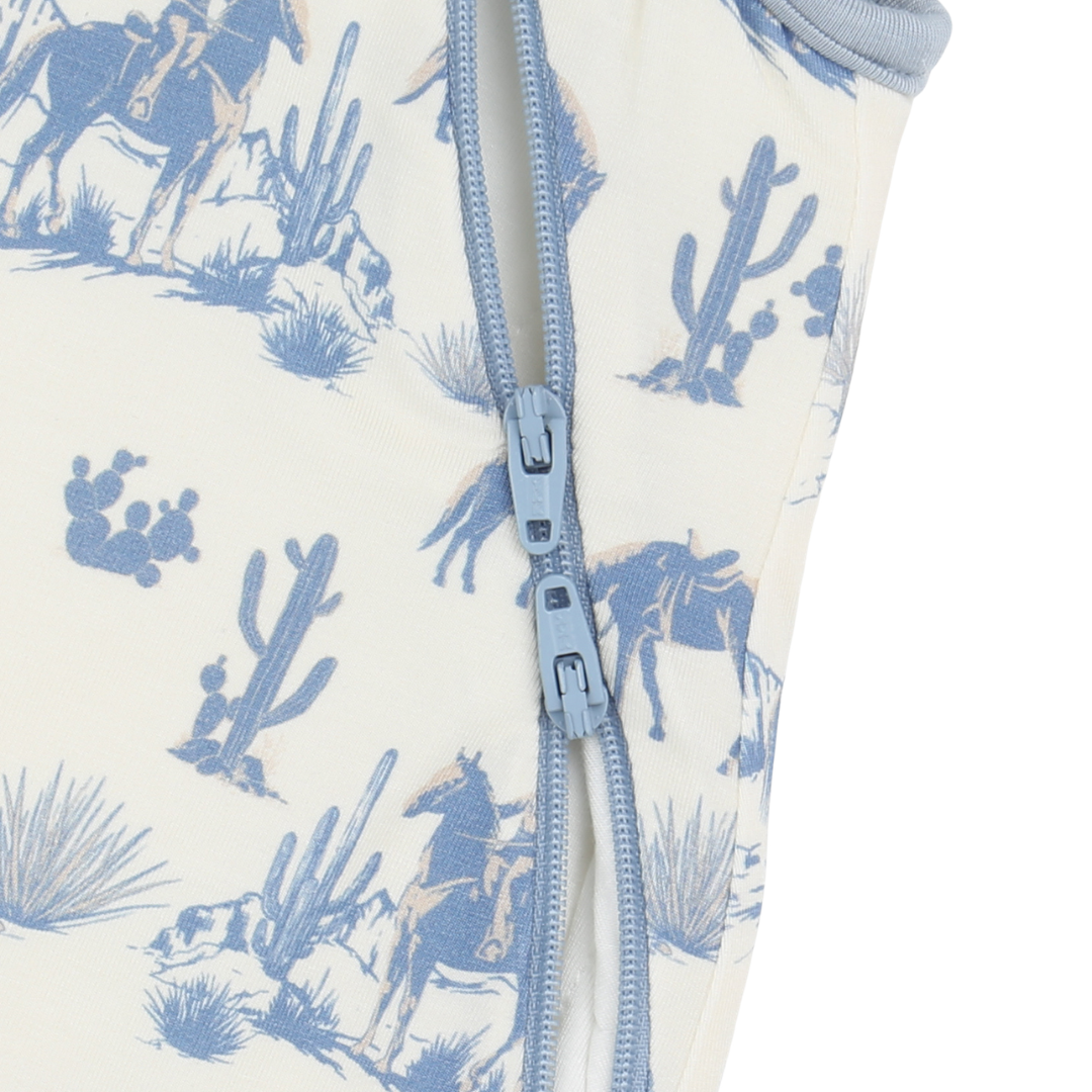 Close-up of a baby onesie with blue desert scene print and zipper.