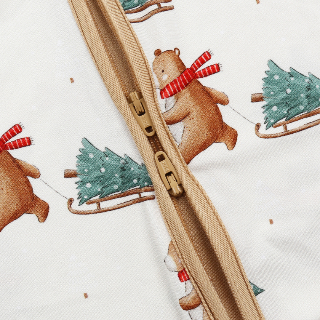 Close-up of a beige zipper on a white fabric background printed with a Christmas bear motif, including brown bears wearing red striped scarves and pulling green Christmas trees in sleds.