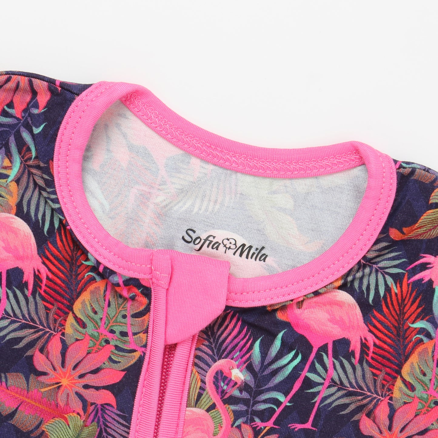 Close-up of a children's outfit with flamingo and leaf pattern and pink neckline, featuring the brand 'Sofia Mila'.