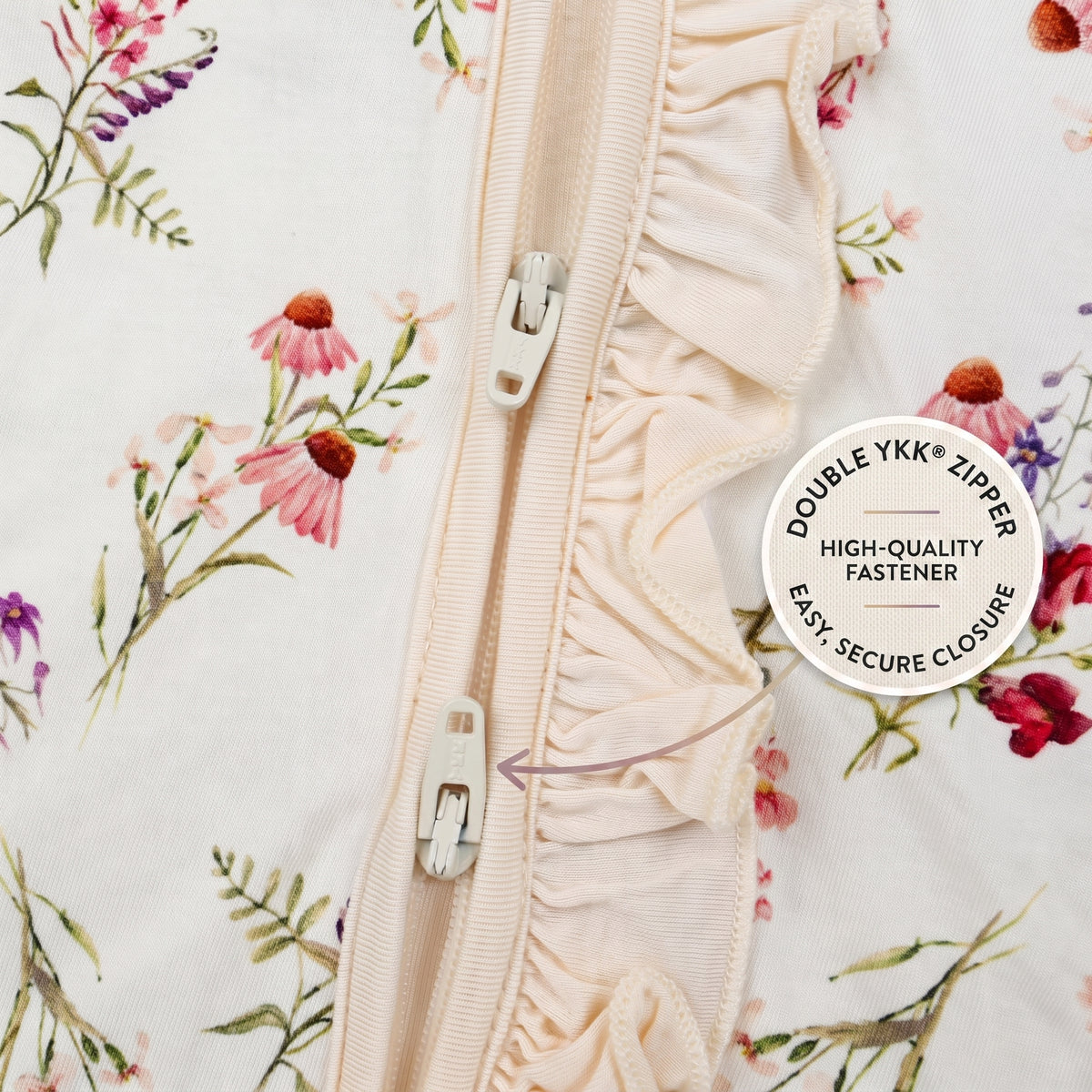 Close-up of a cream-colored ruffled trim with a silver double YKK zipper, set against a white fabric with a pink and green floral print. A circular badge on the right reads 'DOUBLE YKK ZIPPER HIGH-QUALITY FASTENER EASY, SECURE CLOSURE'.