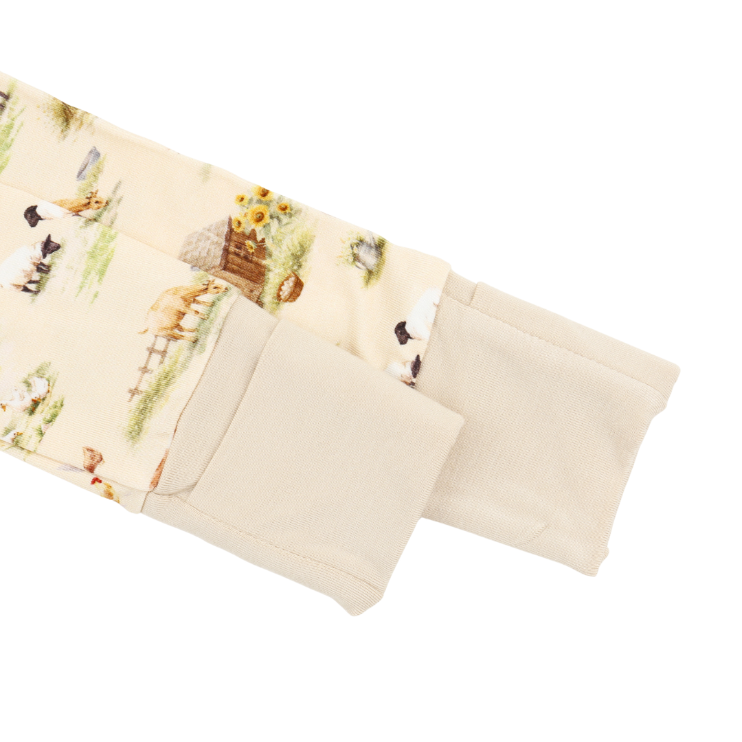 Close-up of a cream-colored sleeve or cuff with a printed pattern of farm animals, flowers, and rustic details, shown against a plain white background.