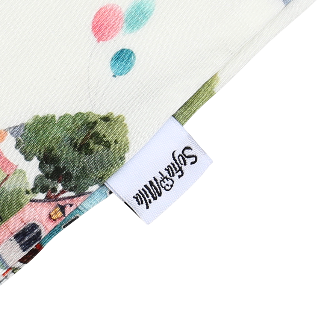 Close-up of a fabric with colorful polka dots and a scenic design, featuring a brand tag.